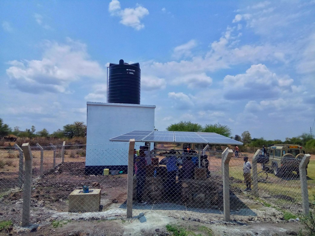 A newly installed set of solar panels next to a well with a pump and water tower