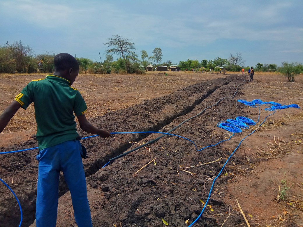 Local helper feeding a long length of blue cable into the protective pipe from neat piles